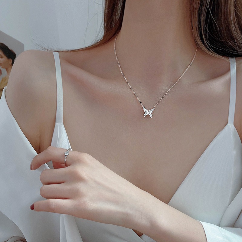 Le cou d'une femme qui porte un débardeur blanc et un collier papillon argenté.
