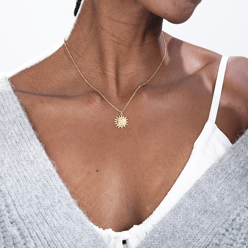 Un cou de femme qui porte un haut blanc et gris et un collier doré autour du cou.