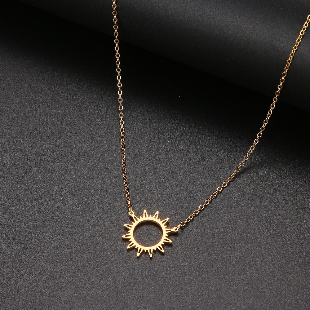 Une collier doré posé sur un fond noir, le pendentif est en forme de soleil.