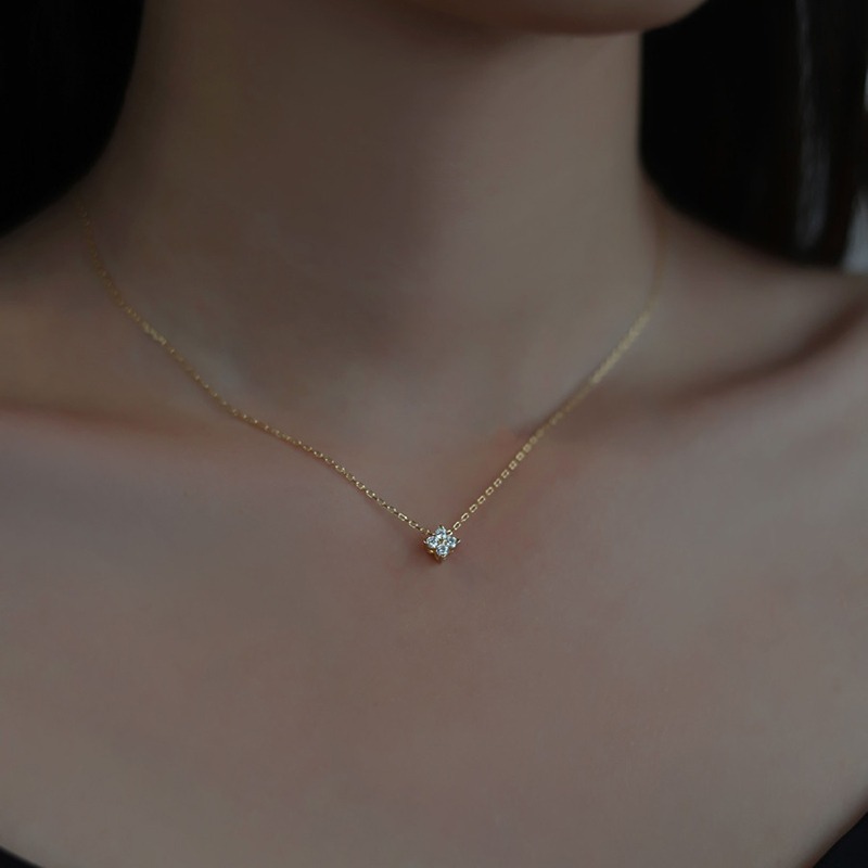 Un collier avec un pendentif trèfle. Le collier est doré, porté autour du cou.